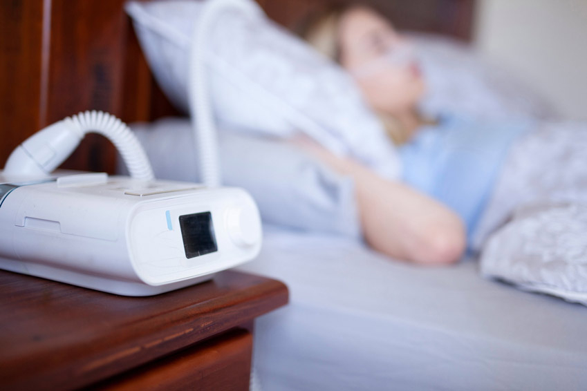 Woman in bed using the CPAP machine on nightstand
